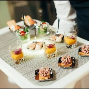 Waitstaff carrying a rectangle light up serving tray with gourmet appetizers at a dimly lit event.