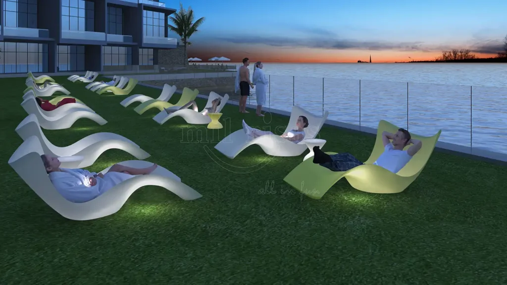 Multiple guests relaxing on glowing led lounge chair units on a resort lawn by the sea at sunset.