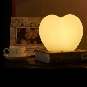 Heart-shaped portable luminaire desk lamp with warm LED glow on a nightstand.