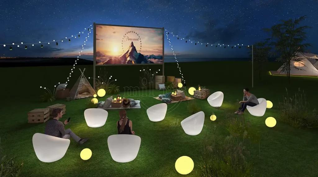 People relaxing in glowing white LED lighted chairs at an outdoor nighttime cinema event.2