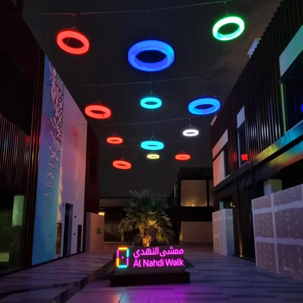Entrance of Al Nahdi Walk featuring a canopy of interactive DMX LED color-changing rings, illuminating the pedestrian path at night.