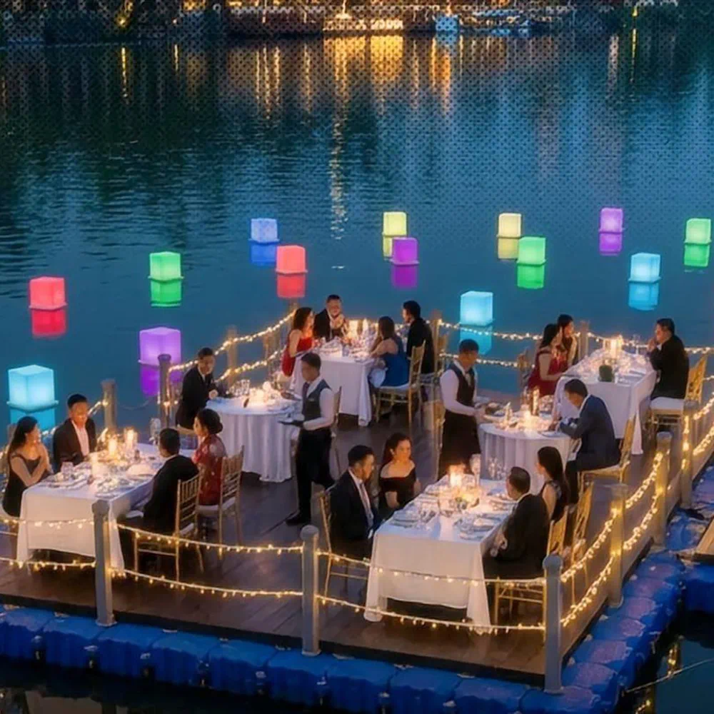 Waterfront Dining with LED Event Decor Furniture, Glowing Cubes, Warm Lighting, and Guests on a Floating Wooden Platform