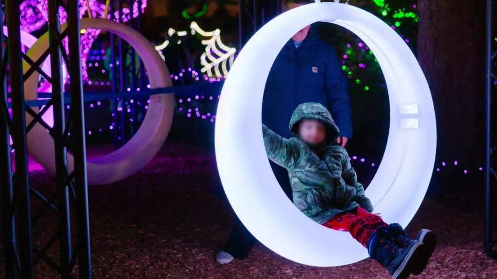 A child enjoying a modern, glowing ring-shaped swing, one of the innovative games with lights at an outdoor evening festival.
