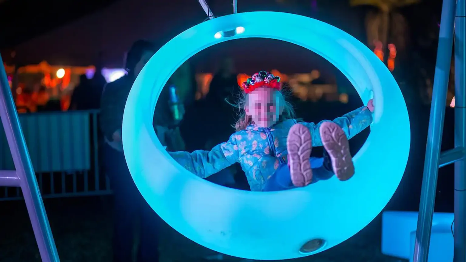 A-child-playing-in-a-glowing-white-LED-circular-swing,-highlighting-interactive-outdoor-entertainment-at-a-night-time-festival.