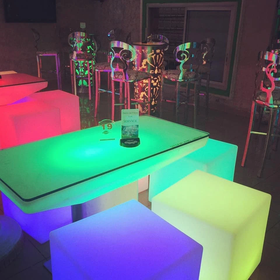 A detailed view of luminous furniture, including a green Large LED High End Table with number 19 sign, surrounded by colorful Glow Cube Seats in a dimly lit lounge