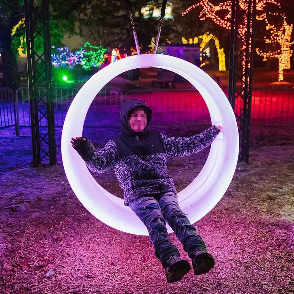 A joyful user enjoying a modern, glowing ring-shaped swing, one of the innovative games with lights at an outdoor evening festival.