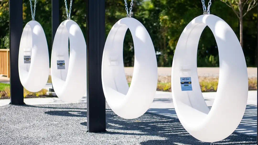 A row of four white LED light up swings hanging over a gray gravel path in an outdoor park