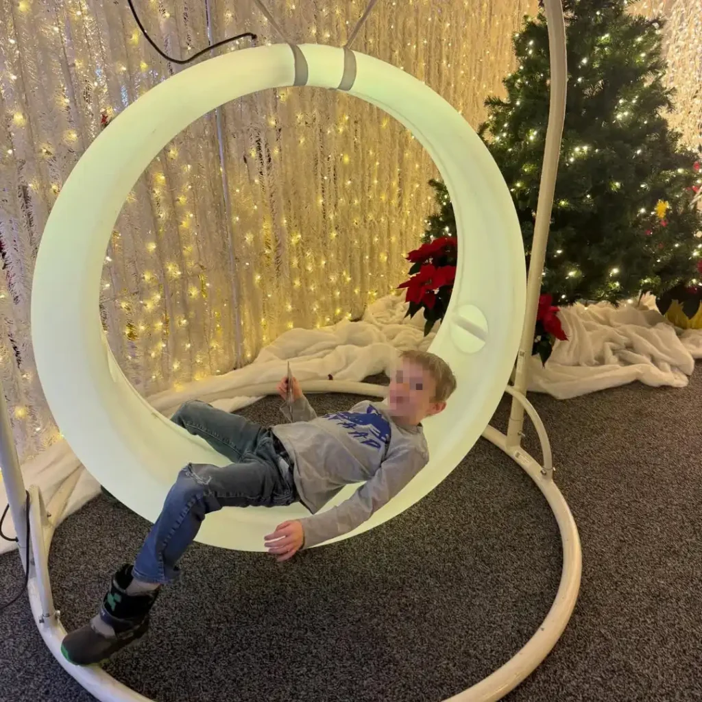 A young boy relaxing in a modern, circular illuminated swing, a featured piece of LED Glow Furniture.