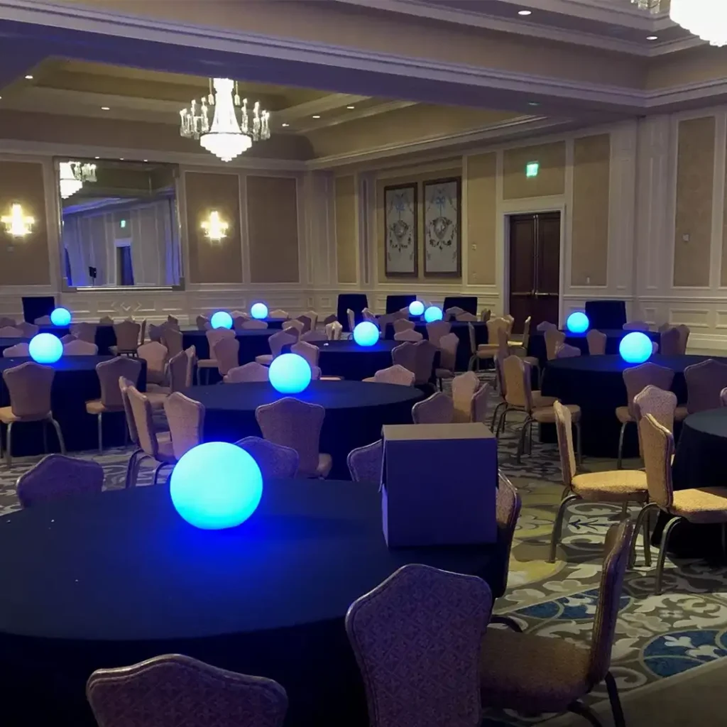 Blue glowing LED balls on black-clothed banquet tables in a large hall with elegant chandeliers.
