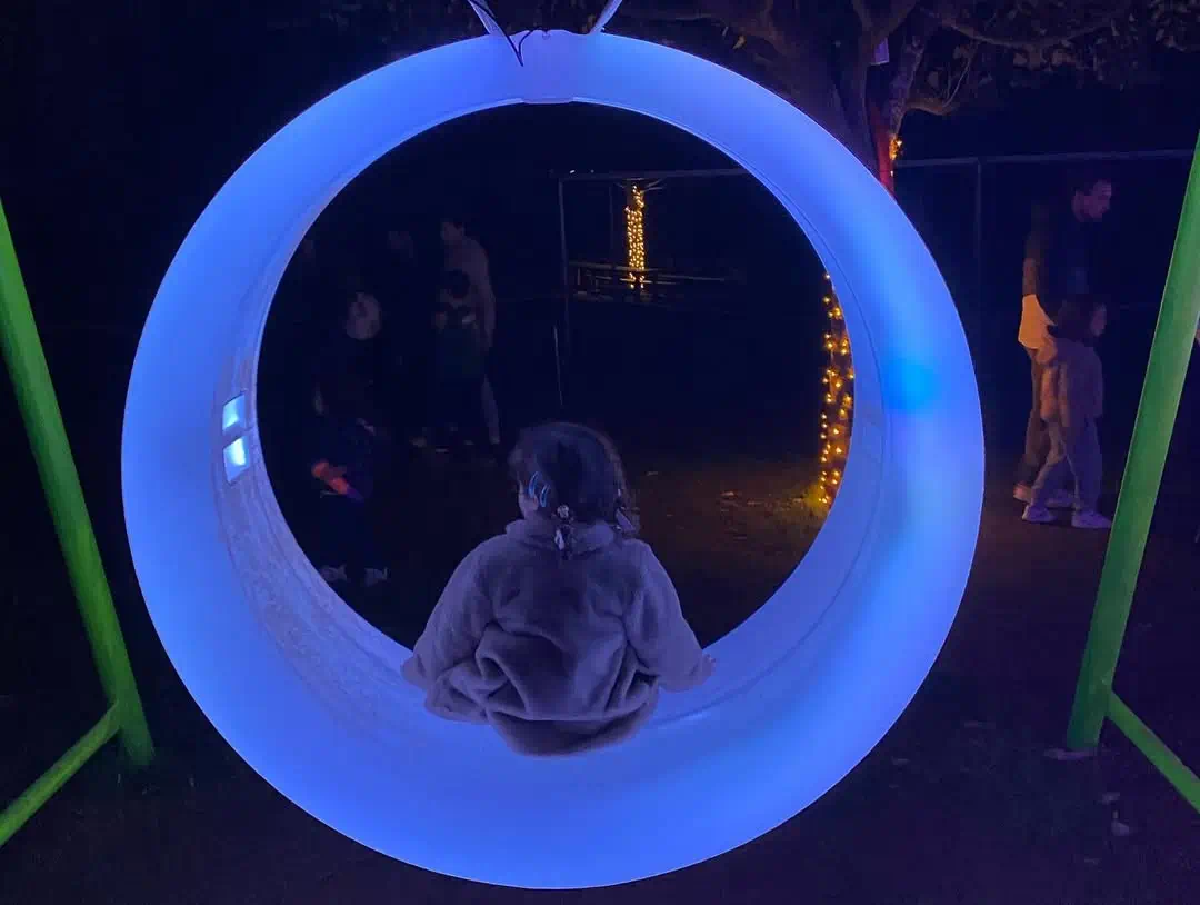 Child enjoying mil risas LED outdoor furniture glow swing with blue LED lights at zoo light festival
