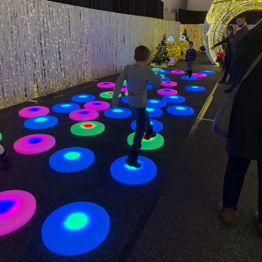 Child jumping on interactive LED Glow Furniture floor tiles with vibrant blue, green, and pink lights in a festive indoor event.