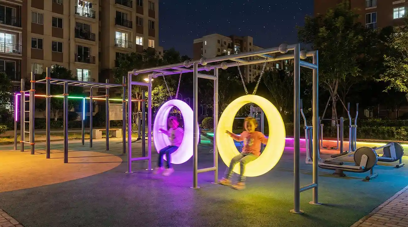 Children playing on glowing Outdoor Round Swing in a community space at night, from LED furniture manufacturer.