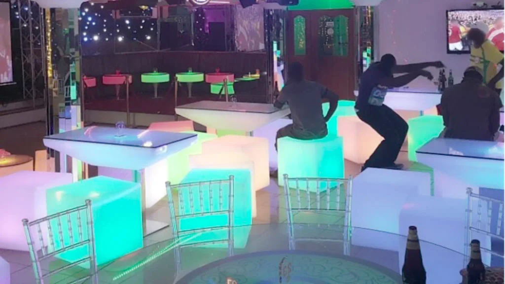 Four people enjoy drinks at a bar, seated around glowing luminous furniture, including rectangular Large LED High End Tables, LED Bar Stools, and small Round LED Tables