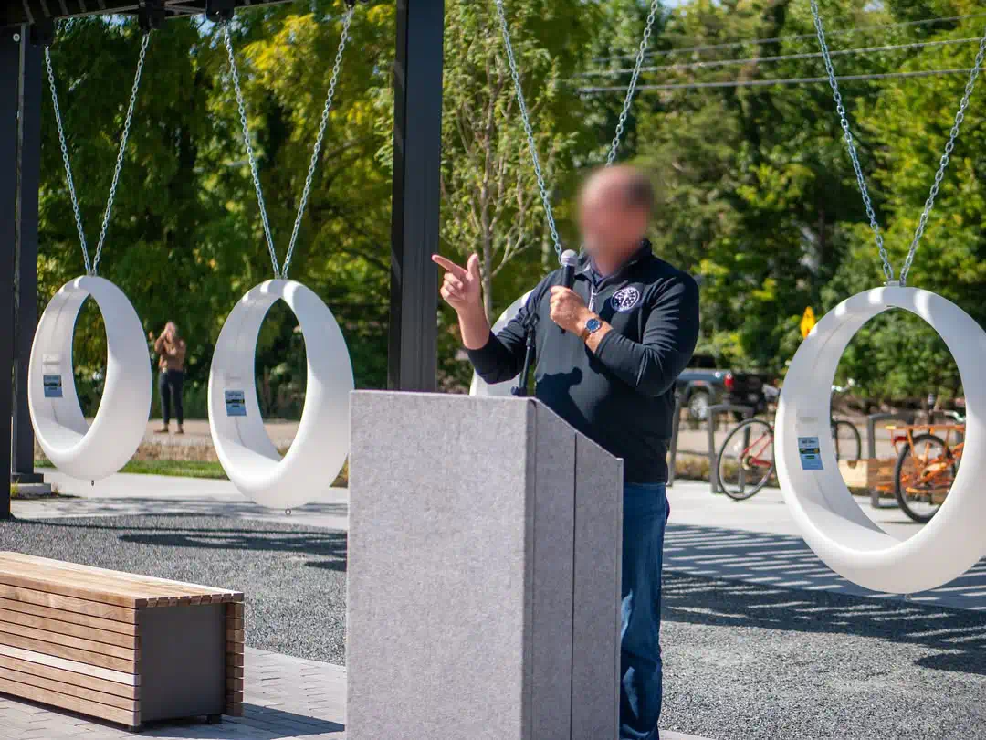 Four white circular LED light up swings hanging behind a speaker at a podium and a wooden bench in an outdoor event