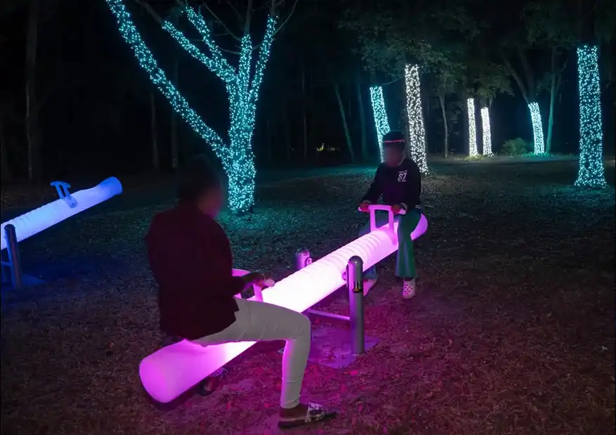 Interactive-Glow-Circular-Swings-collection-illuminating-pink-LED-seesaw-being-used-by-two-people-at-a-night-festival