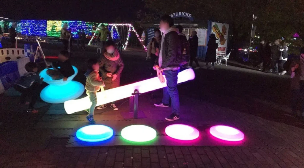 Lighted-furnitures-at-night-featuring-children-playing-with-LED-seesaws,-gyro-chairs,-and-floor-set-on-a-terrace
