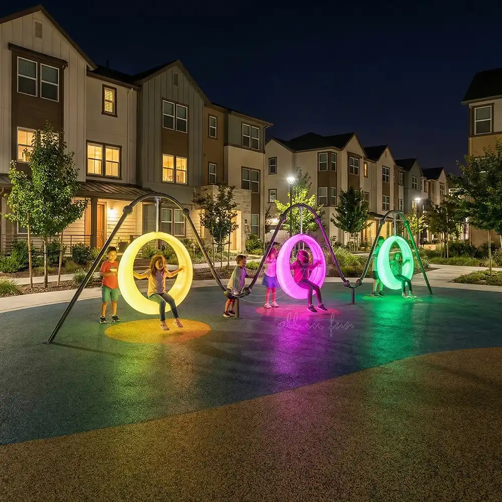 Three vibrant circle swings with yellow, pink, and teal lights installed at a community park at night.