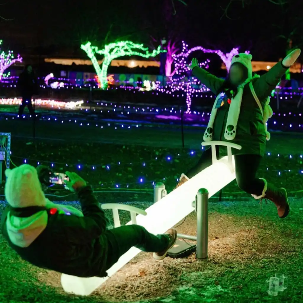 Two people enjoying an interactive glowing LED seesaw, a highlight of outdoor games with lights at a winter night festival.