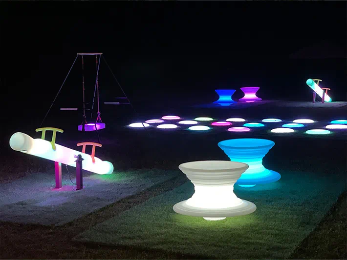 Vibrant lighted furnitures at night, including an LED seesaw, gyro chairs, floor set, and swing on an outdoor terrace
