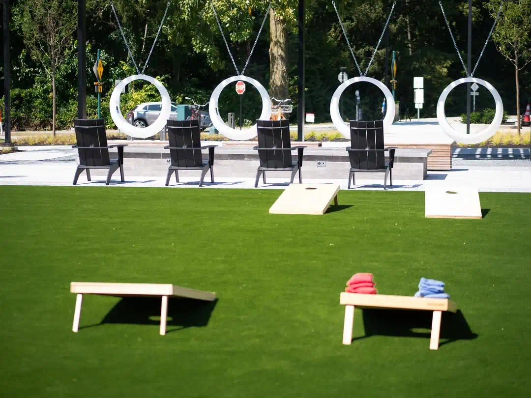 White light up swings behind four black chairs on a green lawn with cornhole boards