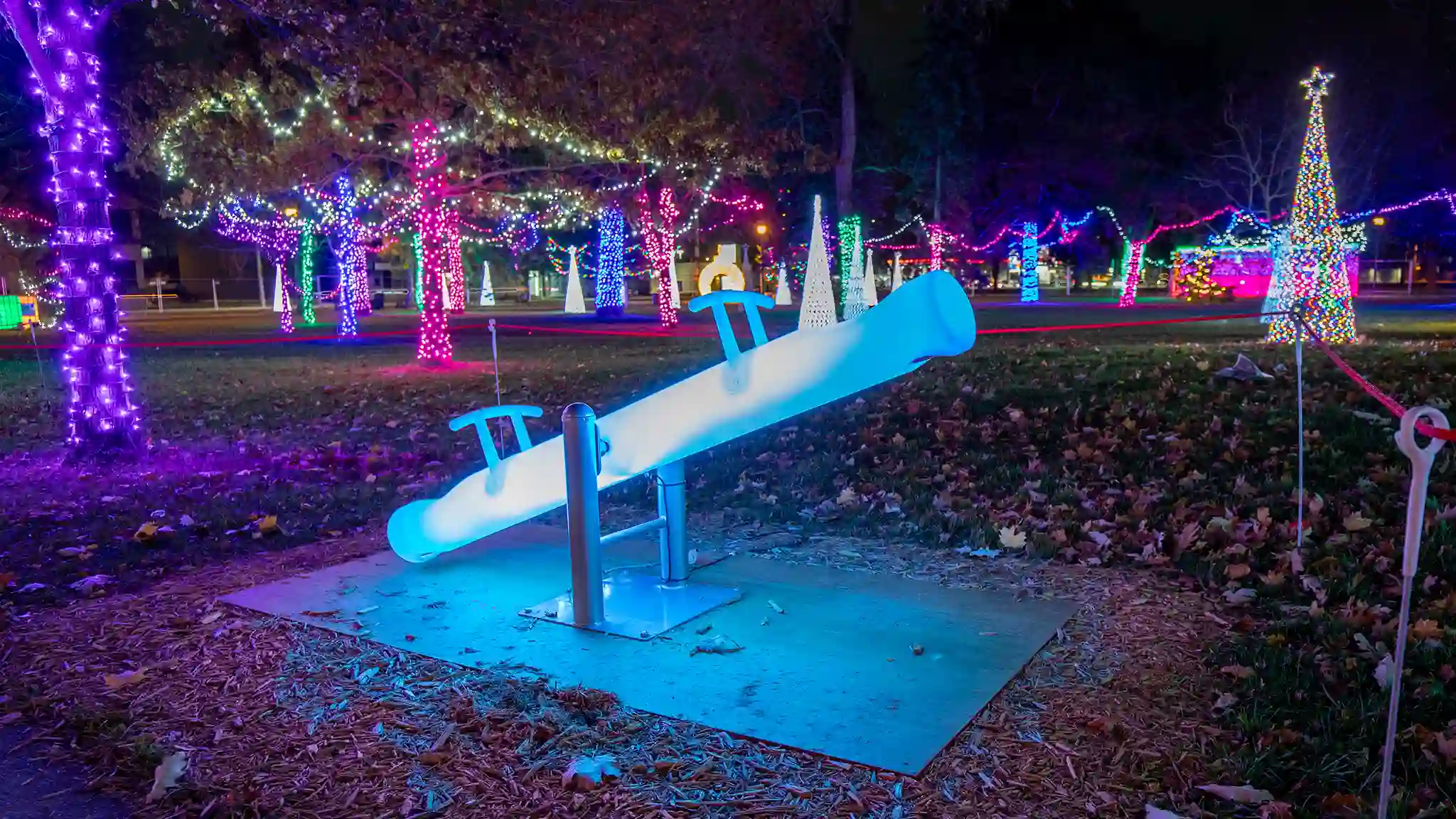 ibrant green illuminated seesaw, part of the LED circle swings collection, creating a magical play experience for kids at a holiday light event.