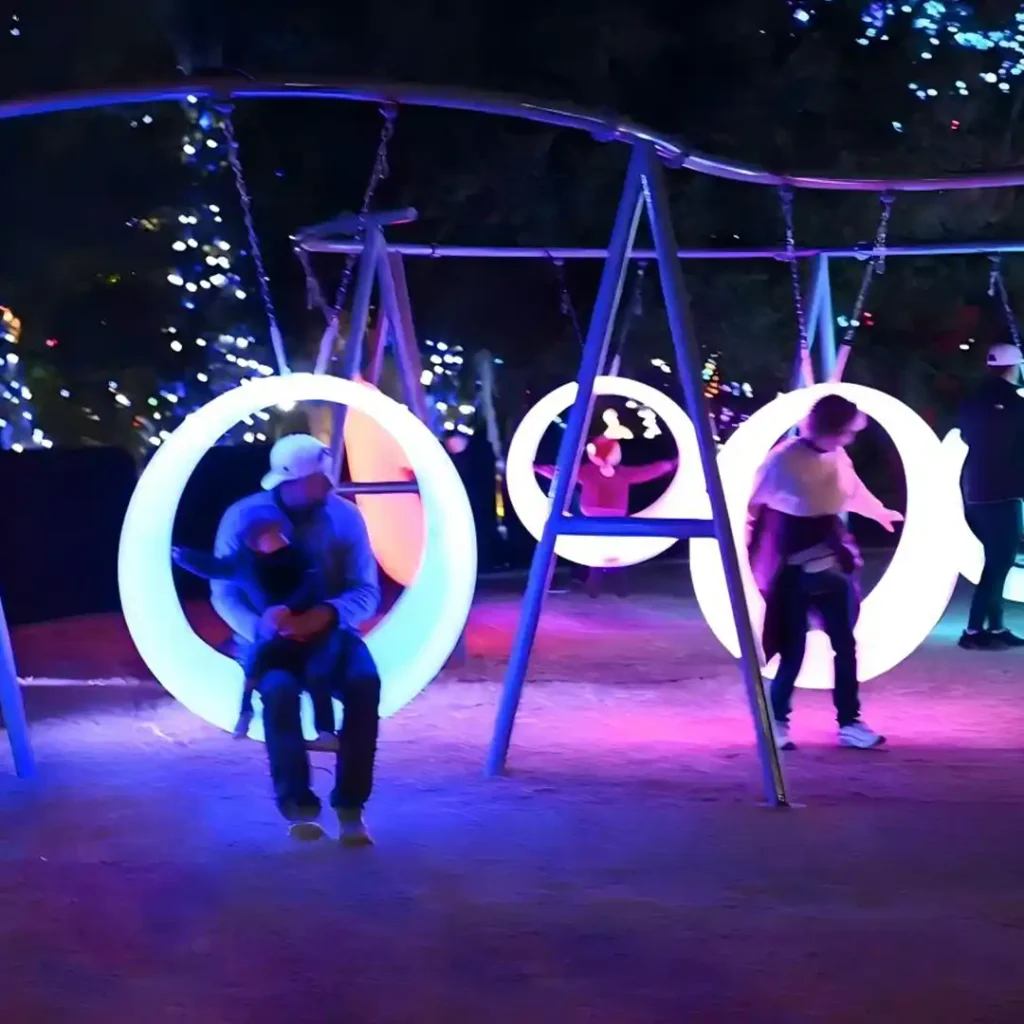 Interactive LED Glow Swings installation by Mil Risas at Phoenix Zoo, featuring glowing circular swings for outdoor playground entertainment.