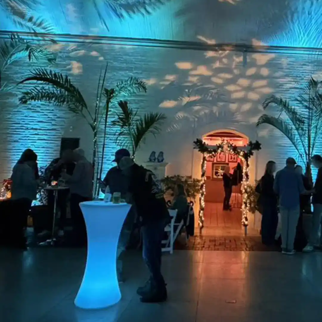 Un groupe de personnes se tient debout autour de tables en forme de sablier illuminées par des LED qui diffusent une lumière bleue vibrante de l'intérieur lors d'un cocktail.