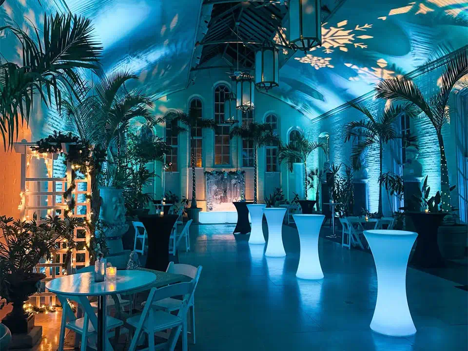 A row of four glowing blue LED lighted tables arranged neatly at an elegant indoor cocktail party