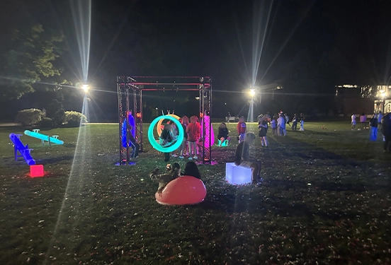 A vibrant New York event featuring lighted games like blue LED seesaws and glowing circular swings, with many guests interacting and playing at night