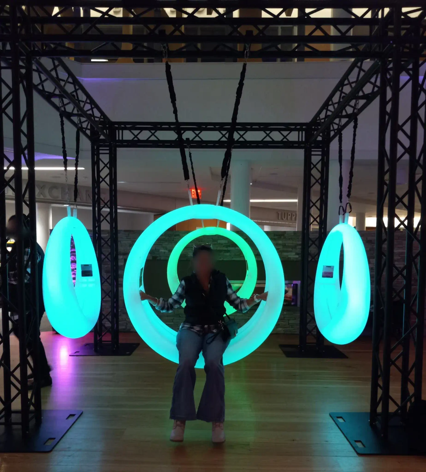 A woman enjoying the lighted games experience on a blue LED circular swing in New York; the event features multiple glowing interactive swings and professional truss structures
