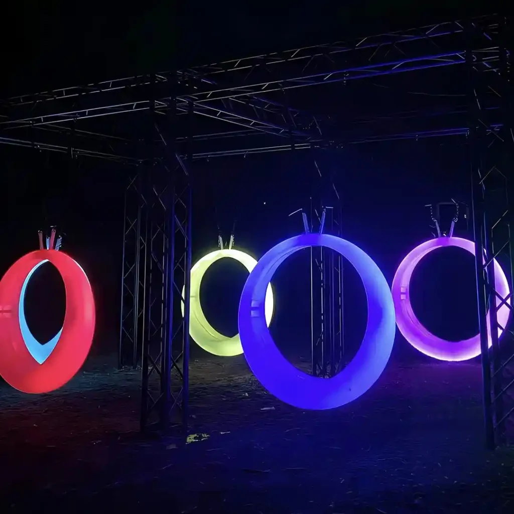 A close-up view of a glowing circular swing with color-changing LED lights at night.