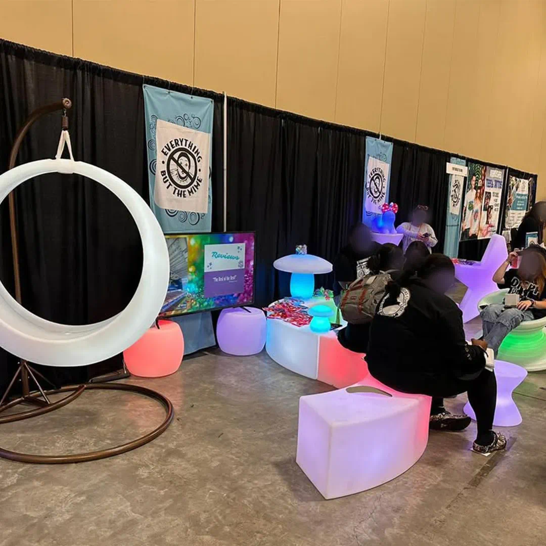 Guests relax on furniture glow products, including an LED swing, curved benches, and mushroom lamps, at a Florida event booth