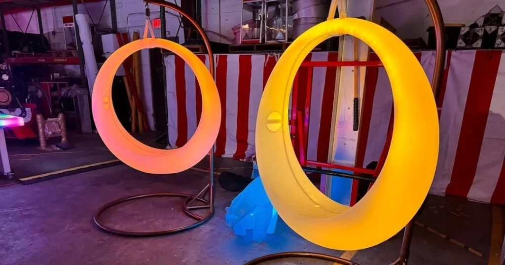 In a Florida warehouse, an orange and a yellow glowing LED Swing (from our furniture glow line) hang in front of a red and white striped backdrop