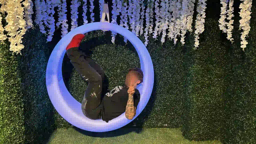 Interactive furniture at Ripley's Aquarium of Texas a visitor posing on a blue illuminated LED swing under floral decor