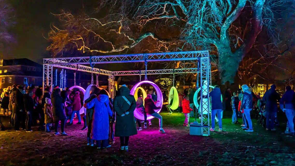 Interactive furniture led lighting installation in Hengelo Netherlands featuring colorful LED swings with tourists playing and taking photos at night