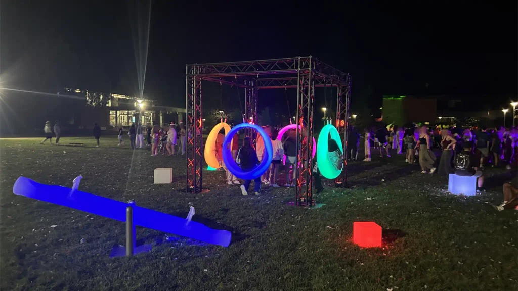 Interactive lighted games in New York featuring blue LED seesaws and multiple colorful glowing swings with guests in a busy outdoor area at night