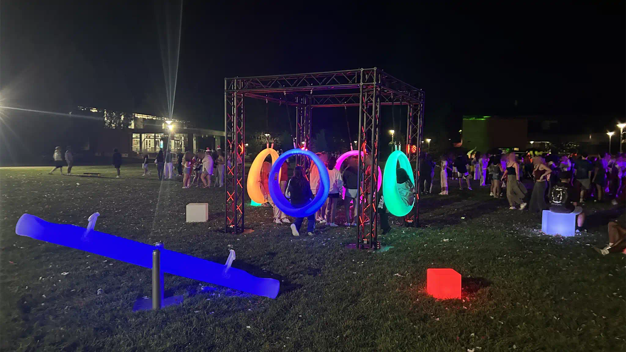 Interactive lighted games in New York featuring blue LED seesaws and multiple colorful glowing swings with guests in a busy outdoor area at night