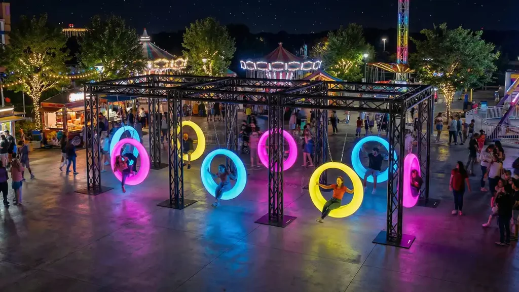 LED Furniture Manufacturer Glowing Outdoor Circle Swing with people at a vibrant amusement park night.