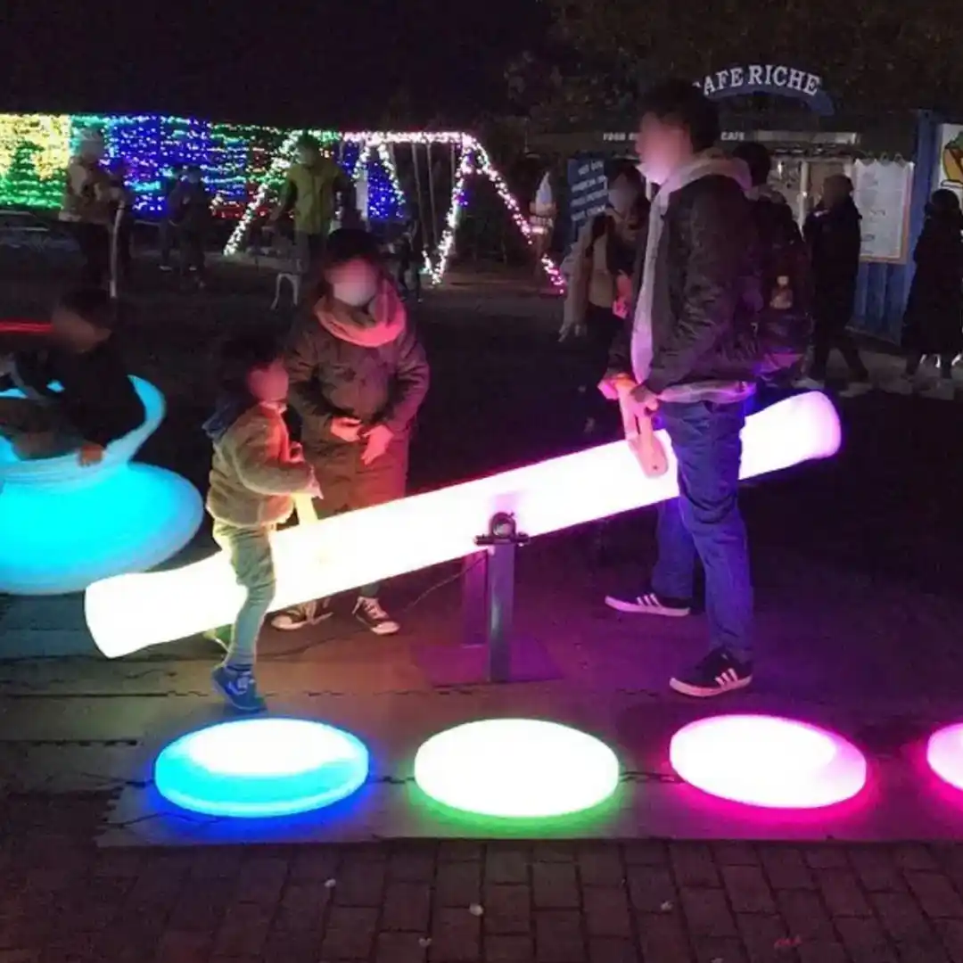 Lighted-furnitures-at-night-featuring-children-playing-with-LED-seesaws-gyro-chairs-and-floor-set-on-a-terrace