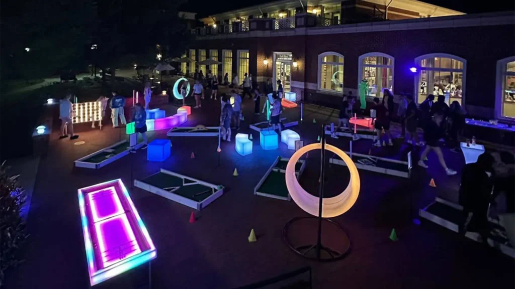 Des personnes profitent d'un événement interactif dans une cour de Floride avec des meubles et des produits lumineux, notamment des balançoires LED, des lampes lapin et des tabourets lumineux.