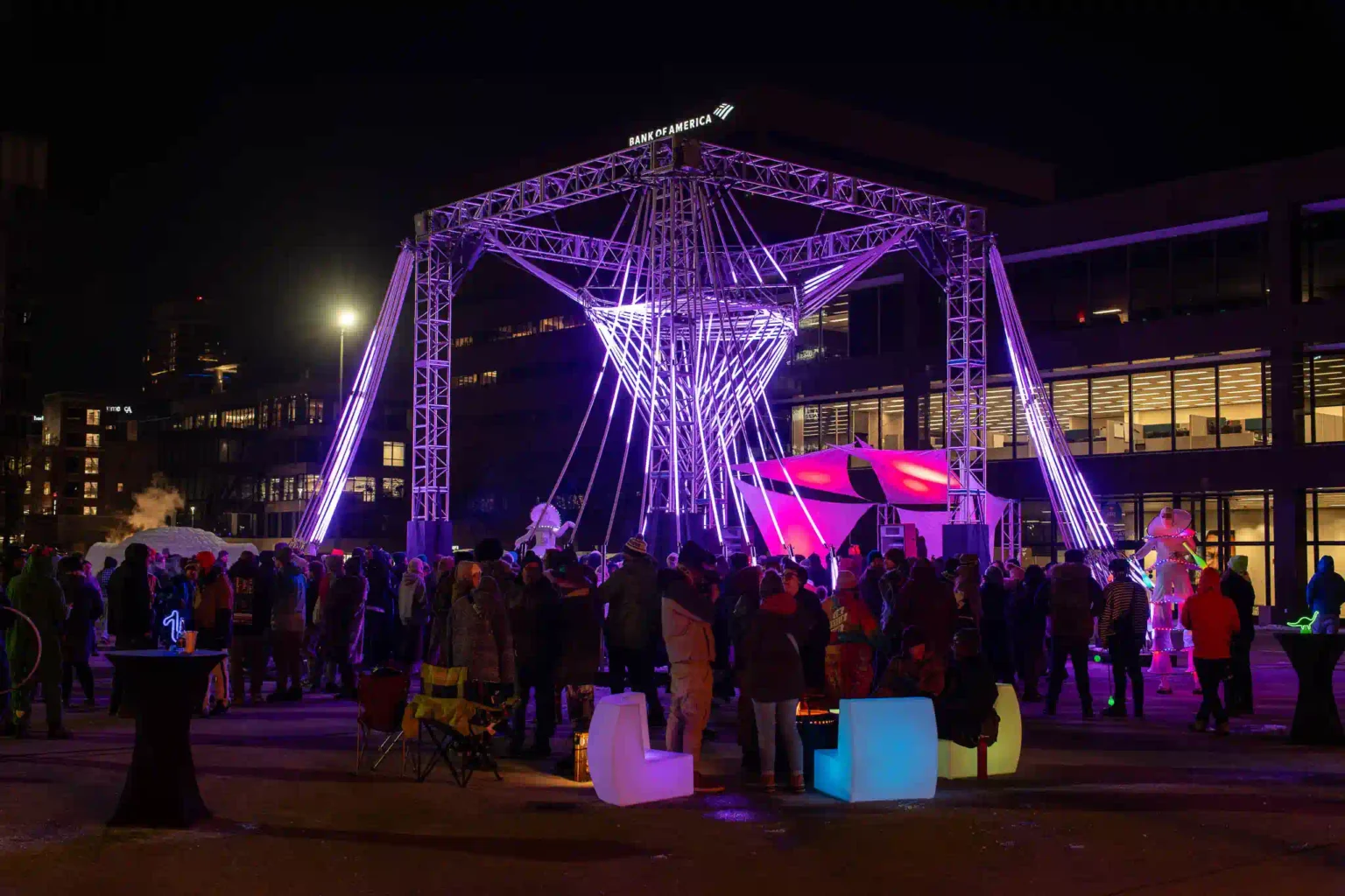 People gather around glowing furniture near a large lit structure at the Michigan World of Winter Festival. lt creating a harmonious festival scene