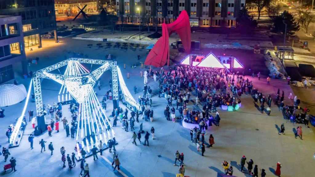 Des visiteurs interagissent avec du mobilier lumineux et coloré, notamment des tables et des canapés d'angle à LED, au Michigan World of Winter Festival, créant une ambiance festive en plein air.
