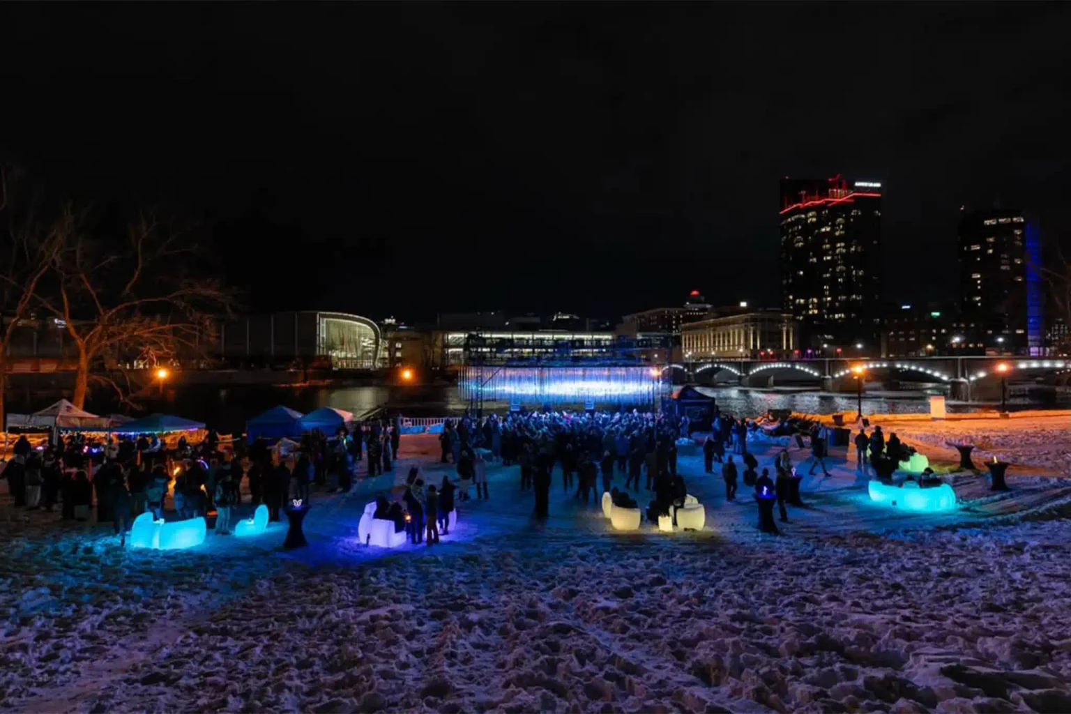 People interacting with weather-resistant glowing furniture, including LED sofas and RGB stools, emitting blue, purple, and yellow light at the Michigan World of Winter Festival