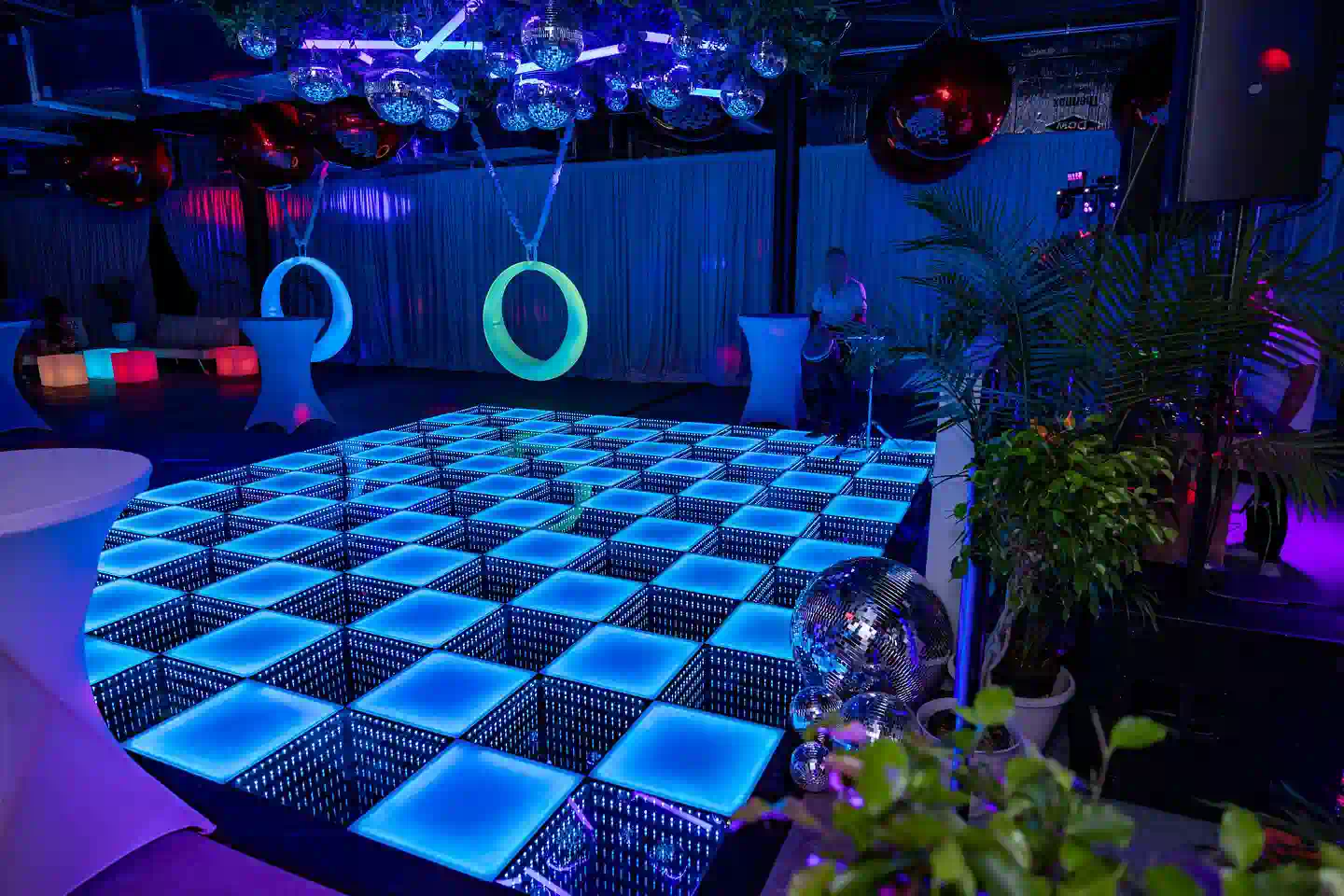 Two weather-resistant swing glow products emitting blue and green light behind an interactive LED dance floor in a Colorado DJ event setup