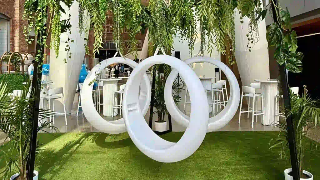 Concept de jeux lumineux avec trois anneaux de balançoire à DEL lumineux sur une pelouse lors d'un événement au Québec, au Canada, une structure de balançoire recouverte de vigne suspendue et des tables et chaises blanches à proximité.