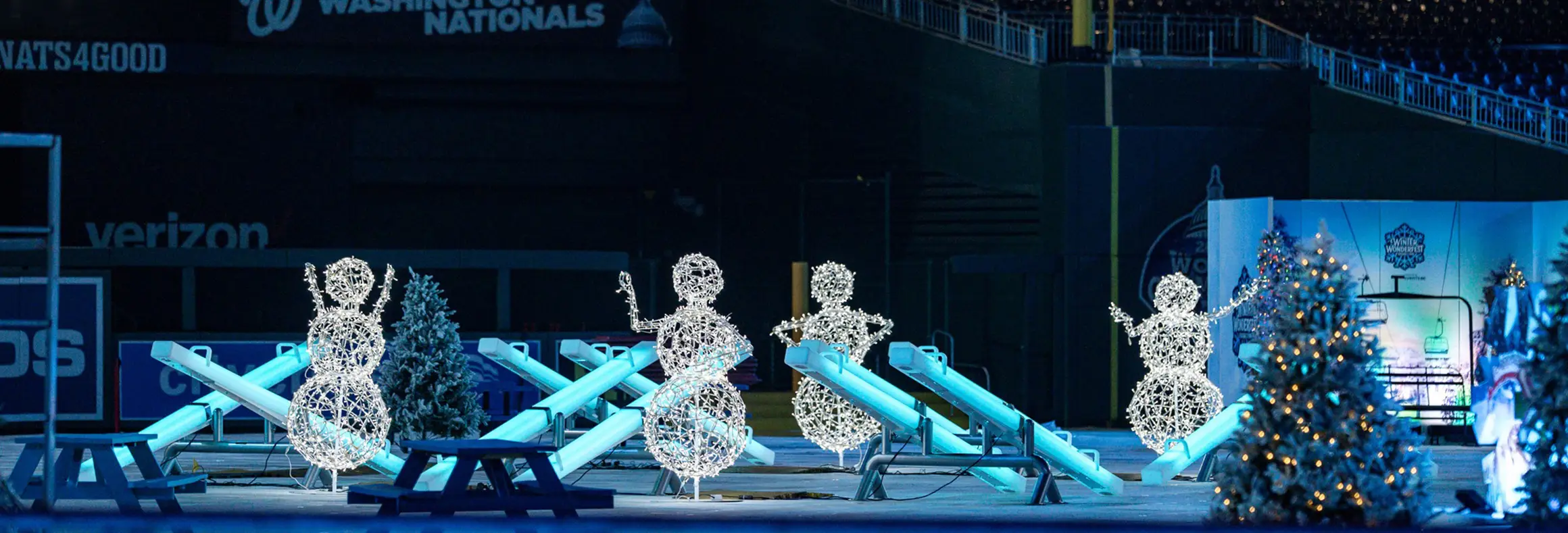 Commercial-grade interactive LED seesaws glowing in blue, installed at a stadium for the Winter Wonderfest event, featuring glowing wireframe snowmen decorations.